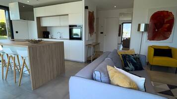 Une cuisine moderne avec des meubles blancs, un four encastré et un coin repas comprenant une table et des chaises blanches.
