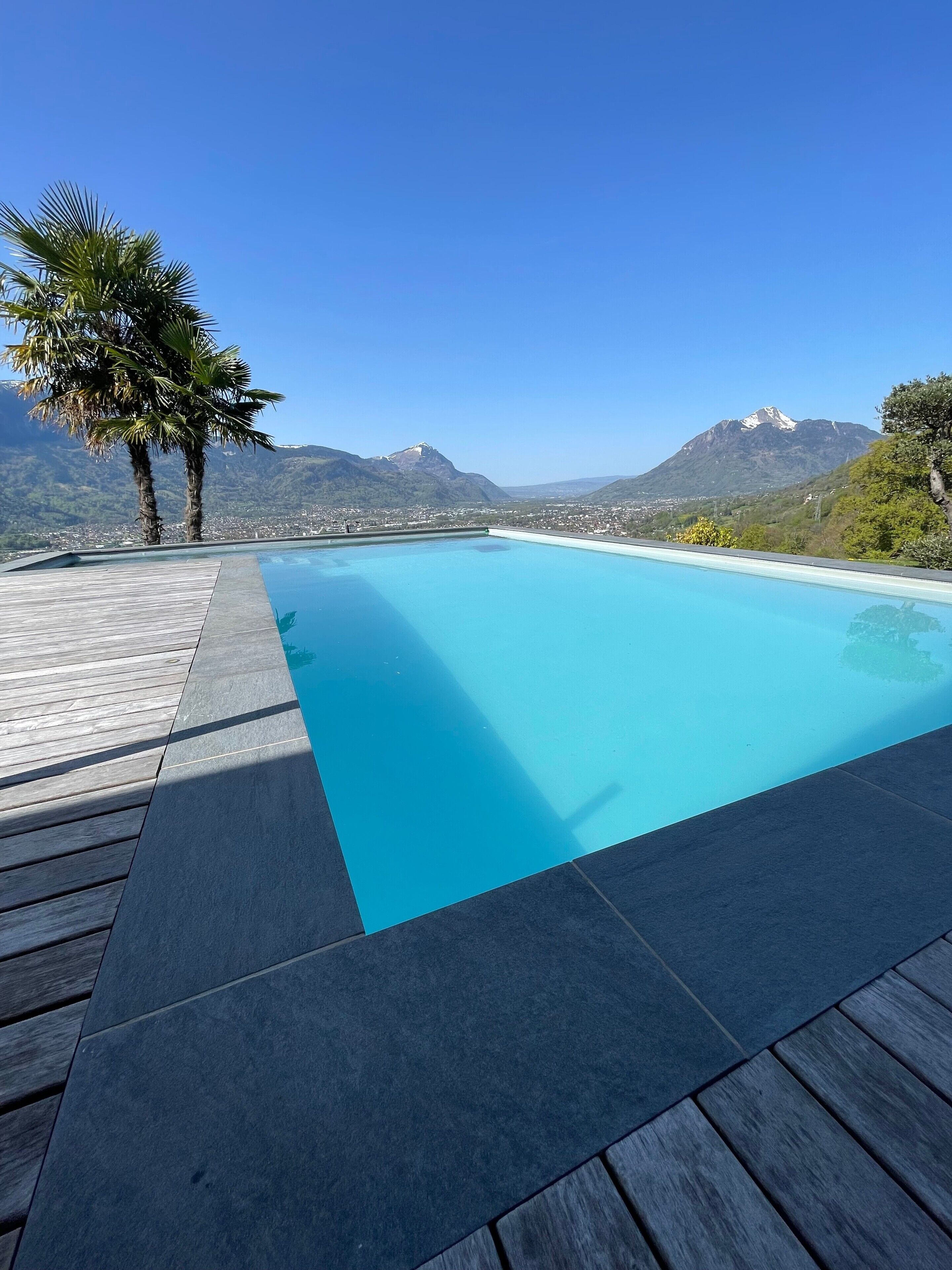 Une piscine rectangulaire dotée d’une terrasse en bois et offrant une vue sur les montagnes.
