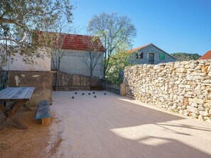 Ein Außenbereich mit einer Steinmauer, einem Holztisch und einem Gebäude mit rotem Dach.
