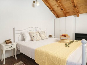 Ein Schlafzimmer mit einem weißen Bett, einem Nachttisch, einem Holz-Kopfteil, einem Kleiderschrank und einem kleinen Tisch mit Früchten.