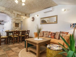 Una sala de estar acogedora con chimenea de piedra, un comedor con sillas de madera, un sofá con cojines estampados y una mesa redonda con un jarrón.