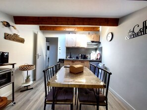 A compact kitchen with wooden cabinets, a dining table with chairs, a clock, and a wall-mounted sign. - Self-contained gîte for 2 people, with kitchen, close to the greenways. (PLAN D ORGON)
