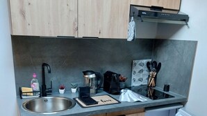 Cuina compacta amb armaris de fusta, un rentamigles d'acer inoxidable, una cafetera i un frigorífic petit.