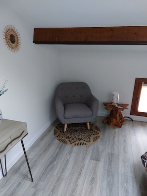 A room with a grey armchair, a round rug, a wooden table, and a unique wooden stool. - Self-contained gîte for 2 people, with kitchen, close to the greenways. (PLAN D ORGON)