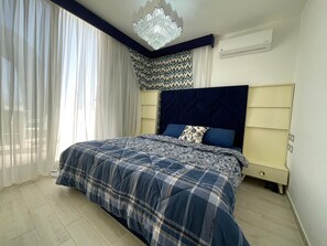 A bedroom with a bed, a chandelier, a nightstand, and a window with sheer curtains. - Fouka North Coast CL4-CH13-03 (Marsa Matrouh)