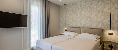 A modern bedroom with a large bed, a flat-screen TV mounted on the wall, and a small round table.
