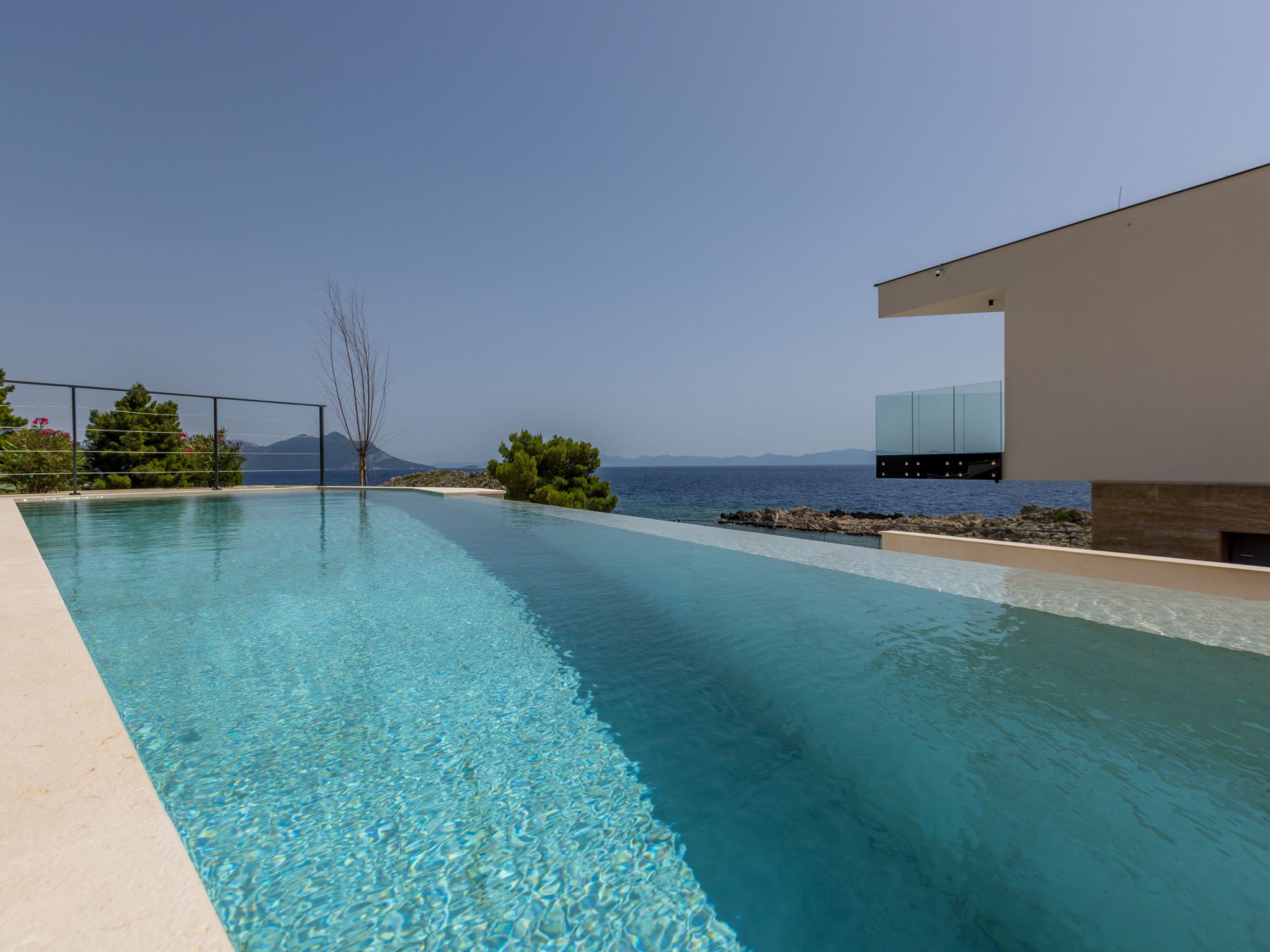 Una piscina blava i nítida amb vistes al mar i a les muntanyes al fons.