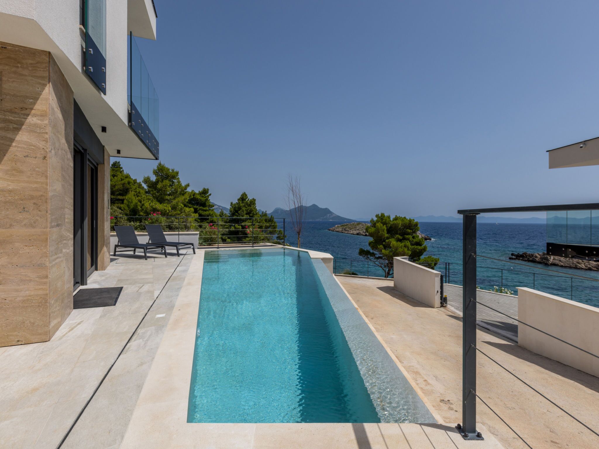 Une piscine extérieure moderne offrant une vue dégagée sur la mer et les montagnes en arrière-plan.