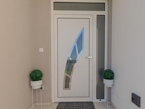 Een moderne deur met een geometrisch patroon in glas, aan weerszijden omlijst door twee potplanten.