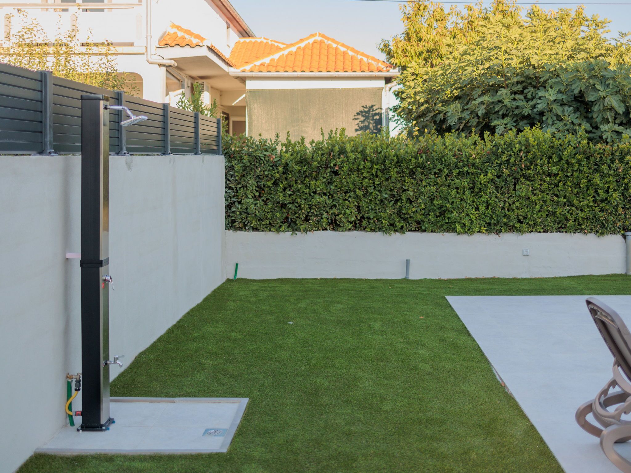 A backyard with artificial grass, a metal fence, and a hedge.