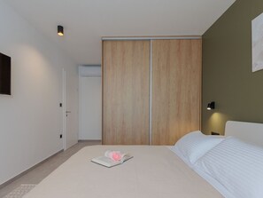Een slaapkamer met een bed, een kledingkast, een nachtkastje en een wandlamp.