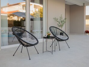 A modern outdoor seating area with two black wicker chairs and a small table, a glass door leading to a pool, and a potted plant. - Stunning Villa Marea with a private pool by Interhome (Vrsi)