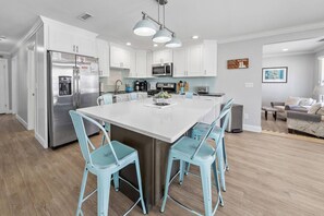 Una cocina moderna con armarios blancos, electrodomésticos de acero inoxidable y una isla central con taburetes de bar.