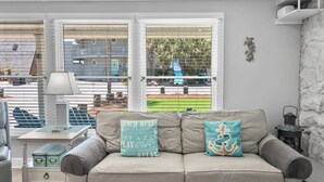 En stue med sofa, to dekorative puder, et bord med lampe og udsigt gennem store vinduer.