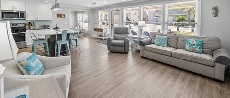 A spacious living area with a sofa, chairs, a dining table, and a kitchen in the background.