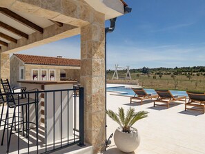 Área à beira da piscina com espreguiçadeiras, bar e vista para um vinhedo.