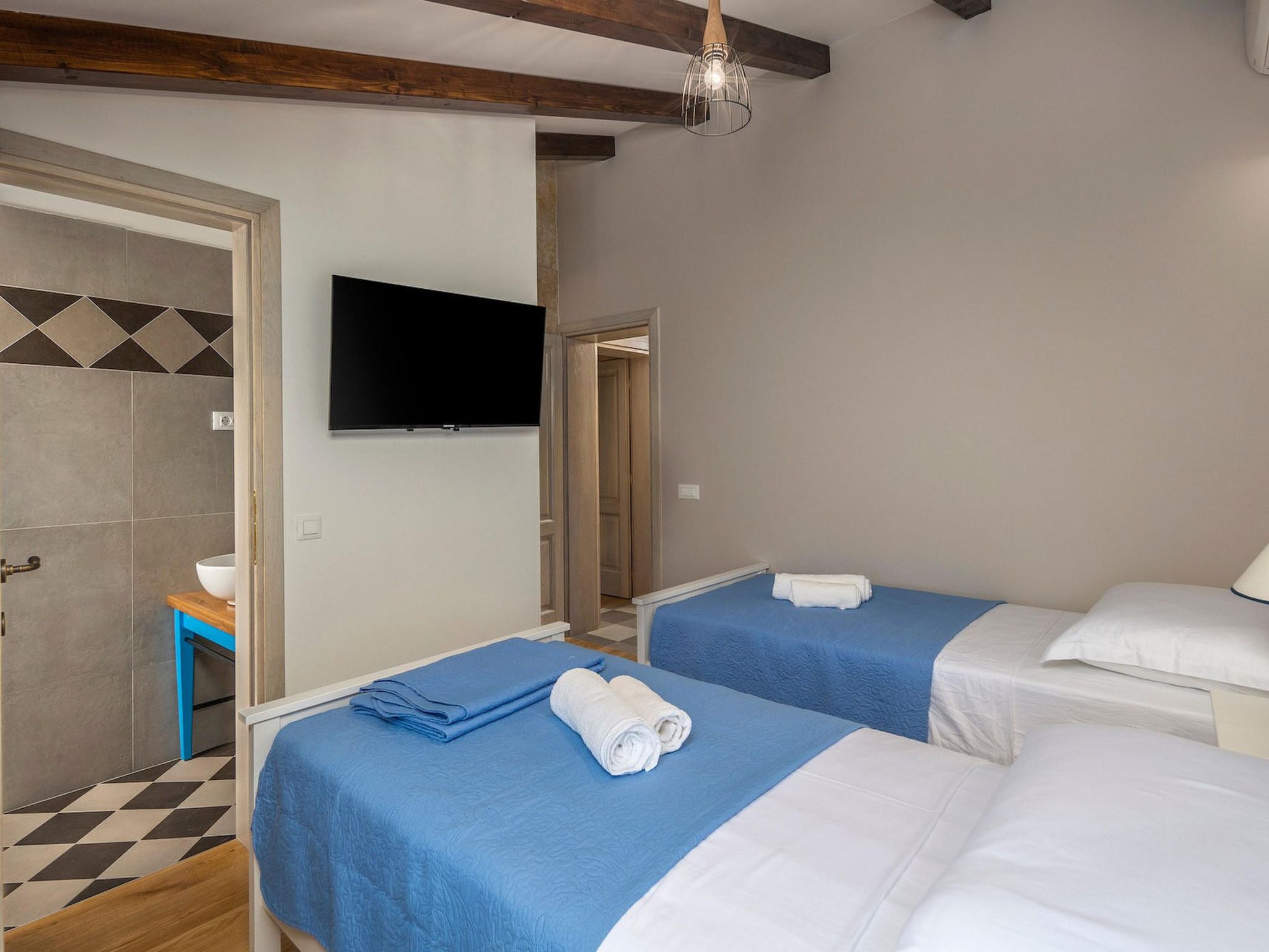 A hotel room with two beds, a TV mounted on the wall, and a bathroom with a tiled floor.