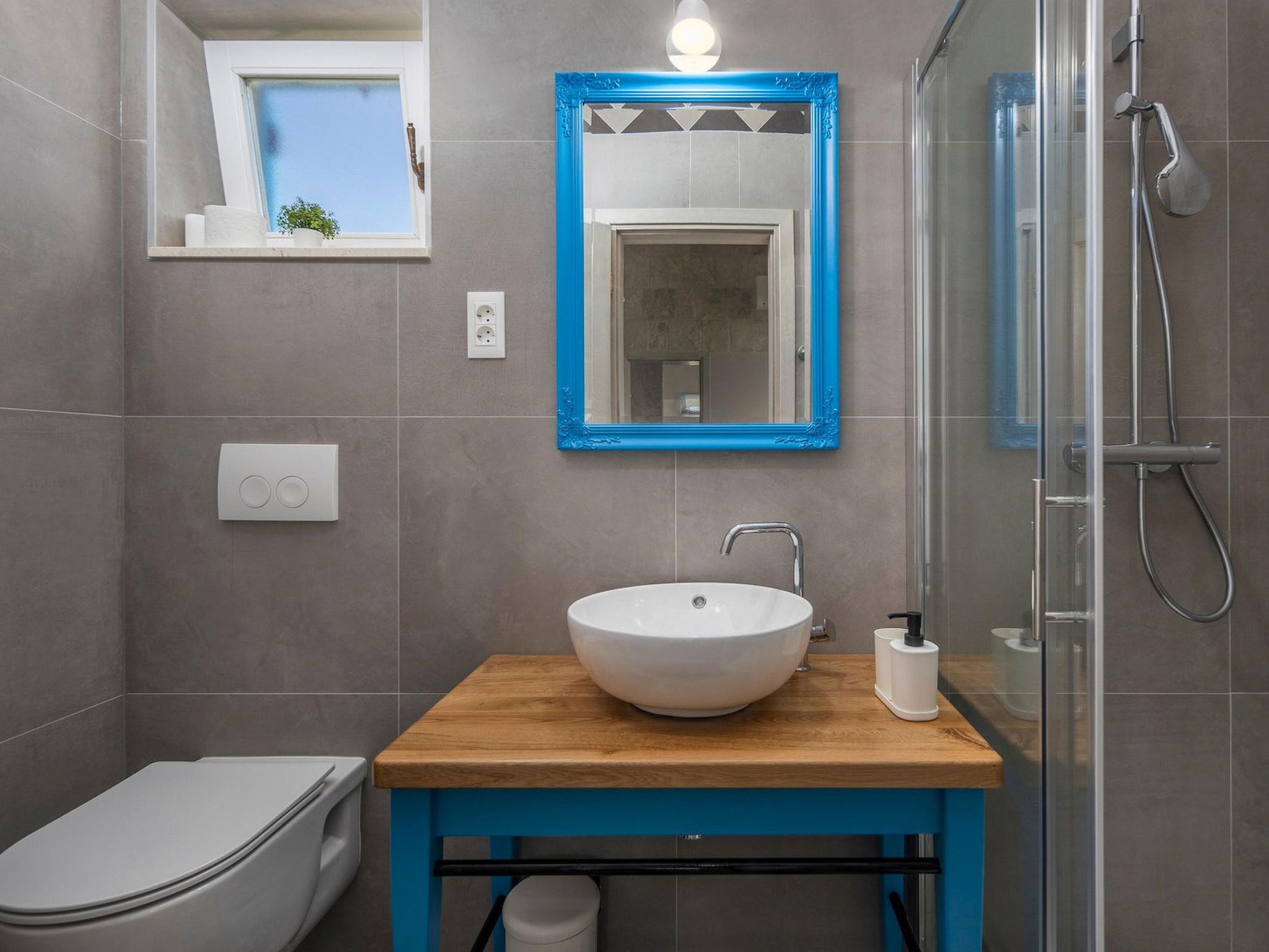 A bathroom with a white sink, a blue-framed mirror, a shower, and a toilet.