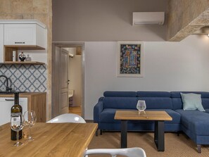 A modern living room with a blue sofa, a wooden coffee table, and a white chair. There is a kitchen area with a wine bottle and glasses on the counter. - Charming villa Viliska with heated pool by Interhome (Donje Rastane)