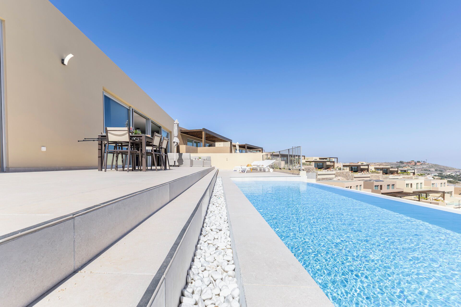 Un espace moderne aménagé au bord de la piscine, offrant une vue dégagée sur la mer, avec un coin repas et un espace salon couvert.