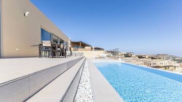Un espace moderne aménagé au bord de la piscine, offrant une vue dégagée sur la mer, avec un coin repas et un espace salon couvert.