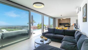 Un salon moderne avec un grand canapé, une table basse et une vue sur la ville et l’océan.