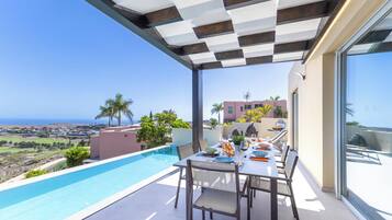 A rooftop terrace with a pool, dining area, and a view of the ocean and hills.