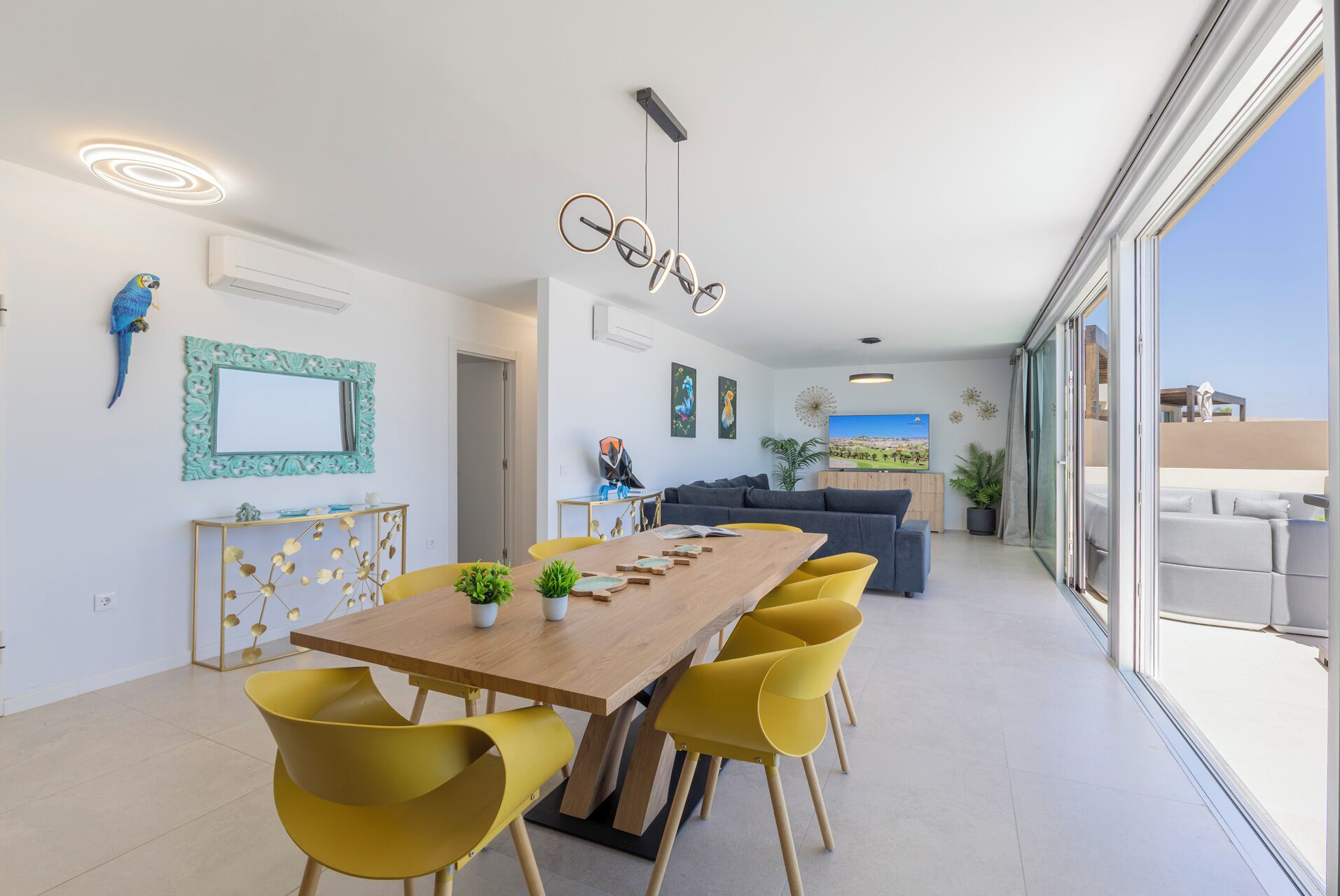 Un espace repas moderne avec une table en bois et des chaises jaunes, un canapé et une grande fenêtre donnant sur un beau paysage.