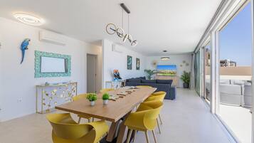 Un espace repas moderne avec une table en bois et des chaises jaunes, un canapé et une grande fenêtre donnant sur un beau paysage.