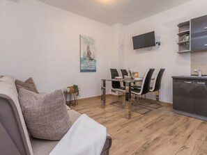 A modern living room with a sofa, a dining table with chairs, a flat-screen TV mounted on the wall, and a kitchen area with cabinets. - Holiday Home Ema with pool by Interhome (Biograd na Moru)