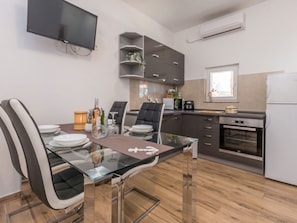 A modern kitchen with a dining area, featuring a glass table, chairs, and a flat-screen TV mounted on the wall. - Holiday Home Ema with pool by Interhome (Biograd na Moru)