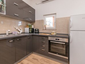 A modern kitchen with dark cabinets, a built-in oven, and a window with a view. - Holiday Home Ema with pool by Interhome (Biograd na Moru)