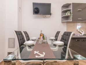 A modern dining area with a glass-top table, four upholstered chairs, and a television mounted on the wall. - Holiday Home Ema with pool by Interhome (Biograd na Moru)