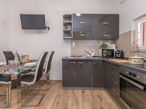 A modern kitchen with a dining area, featuring a flat-screen TV mounted on the wall, a microwave, and a coffee maker. - Holiday Home Ema with pool by Interhome (Biograd na Moru)