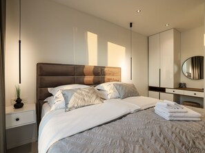 A modern bedroom with a large bed, bedside tables, a dresser, and a mirror. - Villa Barbara with heated pool by Interhome (Drage)