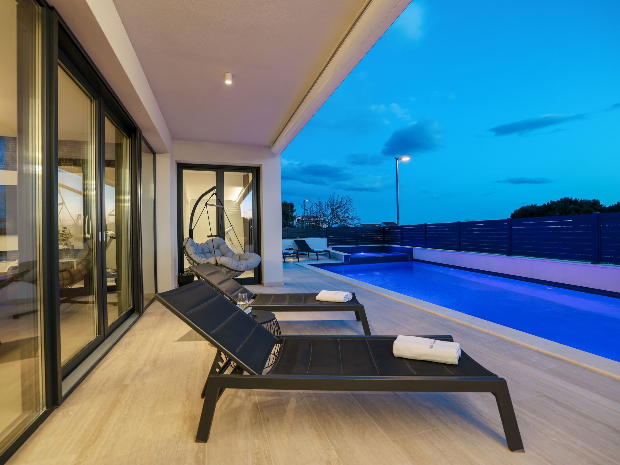 A modern outdoor pool area with lounge chairs and a glass-enclosed room.