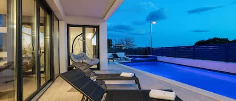 Ein moderner Poolbereich im Freien mit Liegestühlen und einem von Glas umschlossenen Raum.