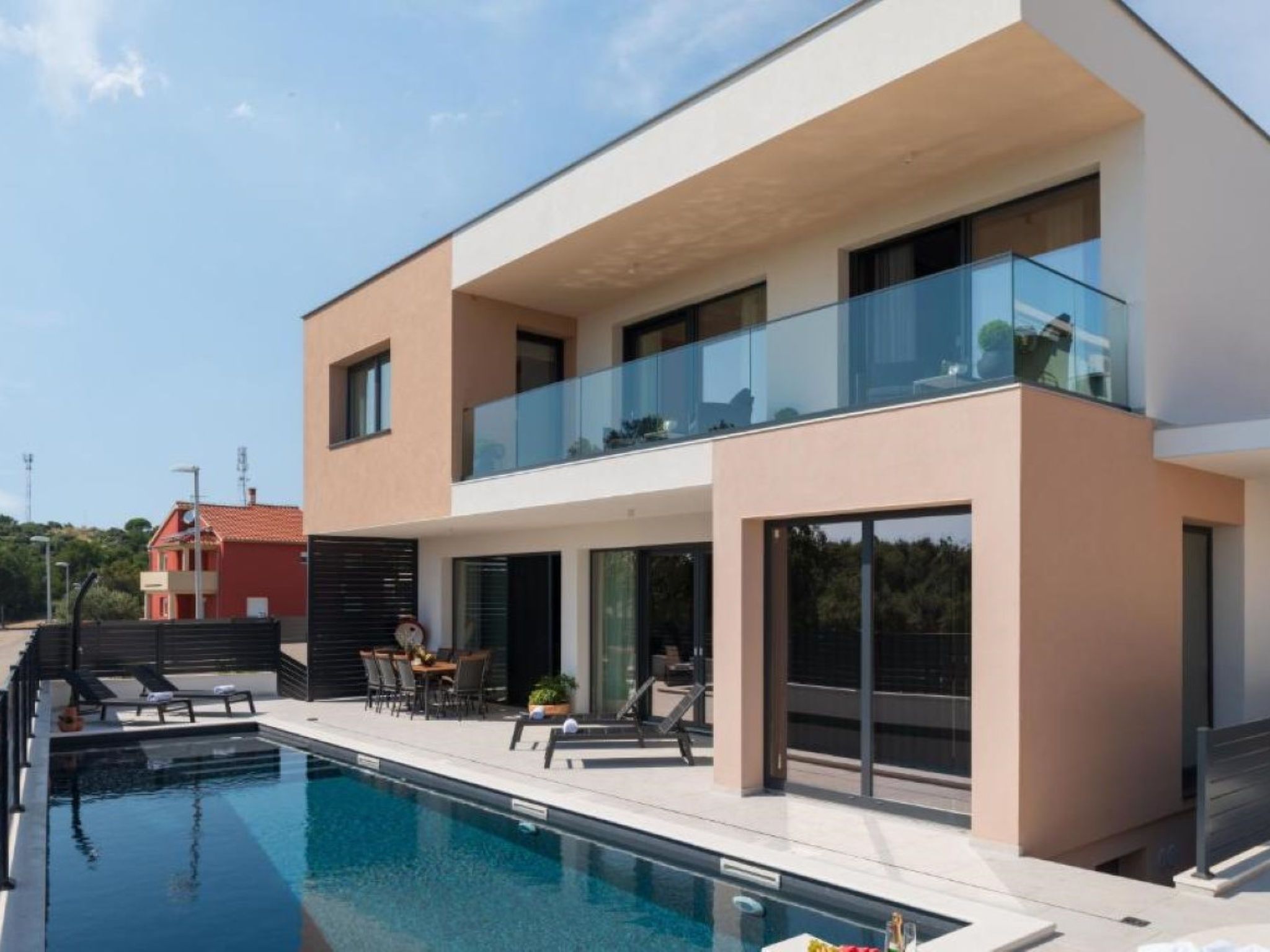 A modern two-story house with a swimming pool, outdoor seating, and a glass balustrade.