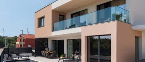 A modern two-story house with a swimming pool, outdoor seating, and a glass balustrade.