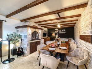 A dining area with a stone fireplace, wooden beams, and a table set for a meal. - Villa Barbara with heated pool by Interhome (Drage)