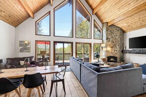A spacious living area with a high ceiling, large windows, a stone fireplace, and a modern sofa. - Ellicottville Escape Chalet, 5 min from town (Salamanca)