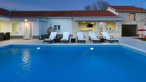 Ein Wohnhaus mit Schwimmbad, Liegestühlen und einer Fassade aus Naturstein.