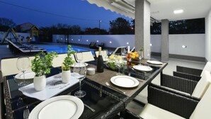 Ein Essbereich im Freien mit Blick auf einen Pool, Tische gedeckt mit Tellern und Gläsern, und eine Pergola darüber.