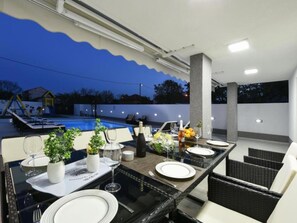 An outdoor dining area with a pool view, tables set with plates and glasses, and a pergola overhead. - Villa Mare with heated pool and gym by Interhome (Crno)