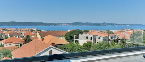 Un barrio residencial con tejados de tejas rojas, cielo azul despejado y vistas al mar y colinas lejanas.
