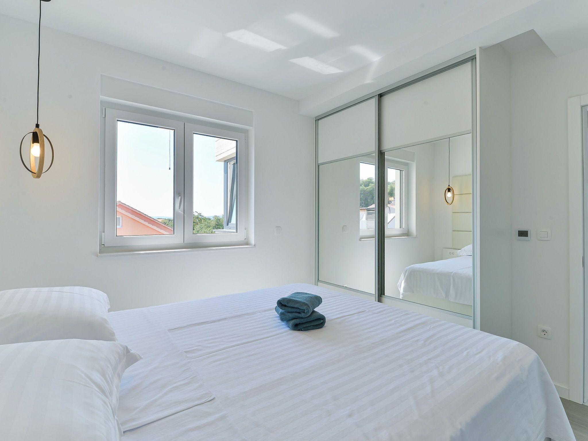 Ein Schlafzimmer mit einem Bett, einem Fenster, einem Spiegel und einer Pendelleuchte.