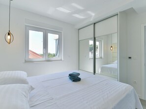 A bedroom with a bed, a window, a mirror, and a hanging light fixture. - Apartment  by Interhome (Zadar/Bibinje)