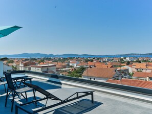A rooftop terrace with a table and chairs, overlooking a coastal town with red-roofed buildings and a clear blue sky. - Apartment  by Interhome (Zadar/Bibinje)