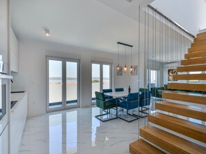 A spacious living area with a modern staircase, large windows, and a dining set. - Apartment  by Interhome (Zadar/Bibinje)