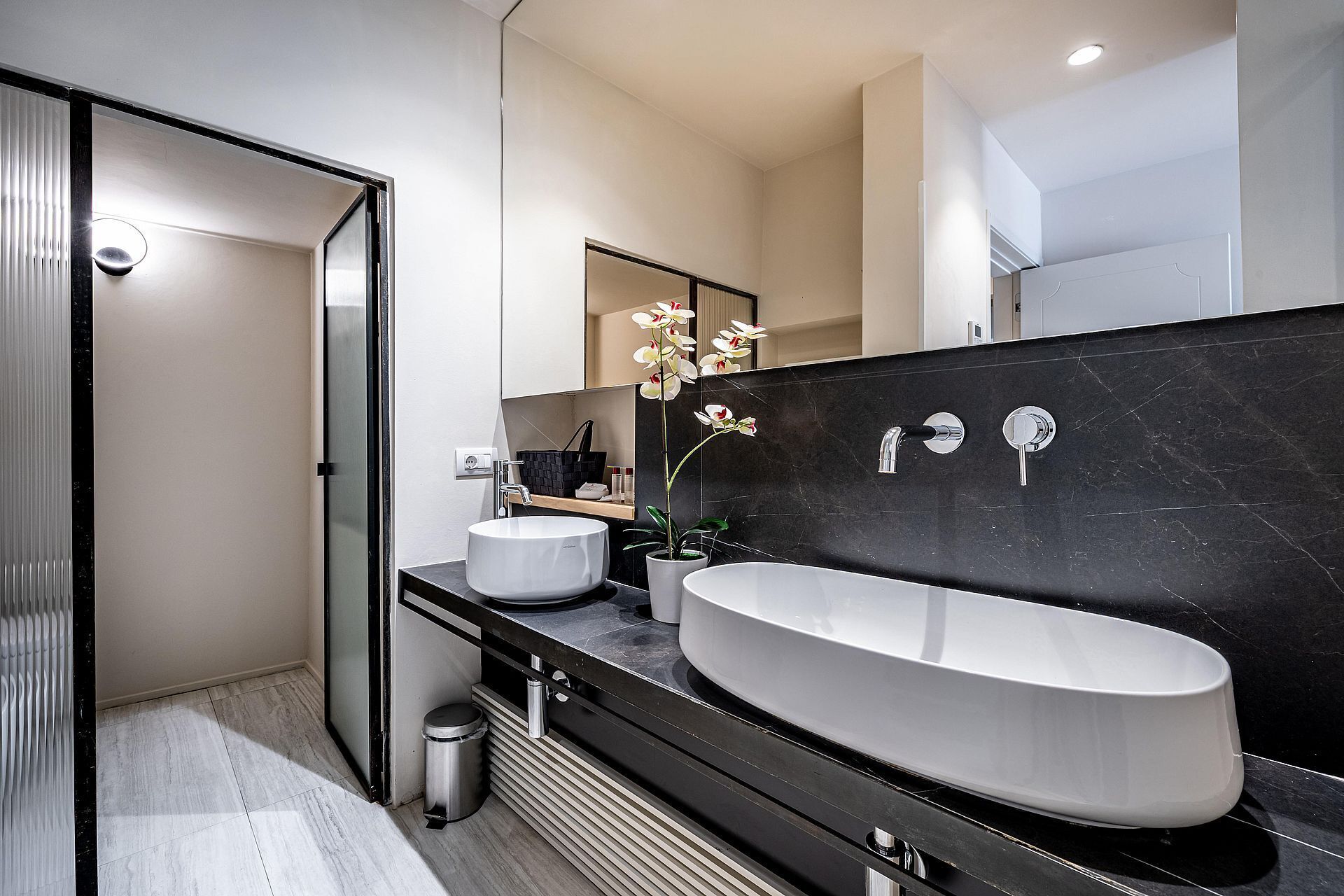 Ein modernes Badezimmer mit einem großen, ovalen Waschbecken, zwei Spiegeln und einer Rückwand aus schwarzem Marmor.